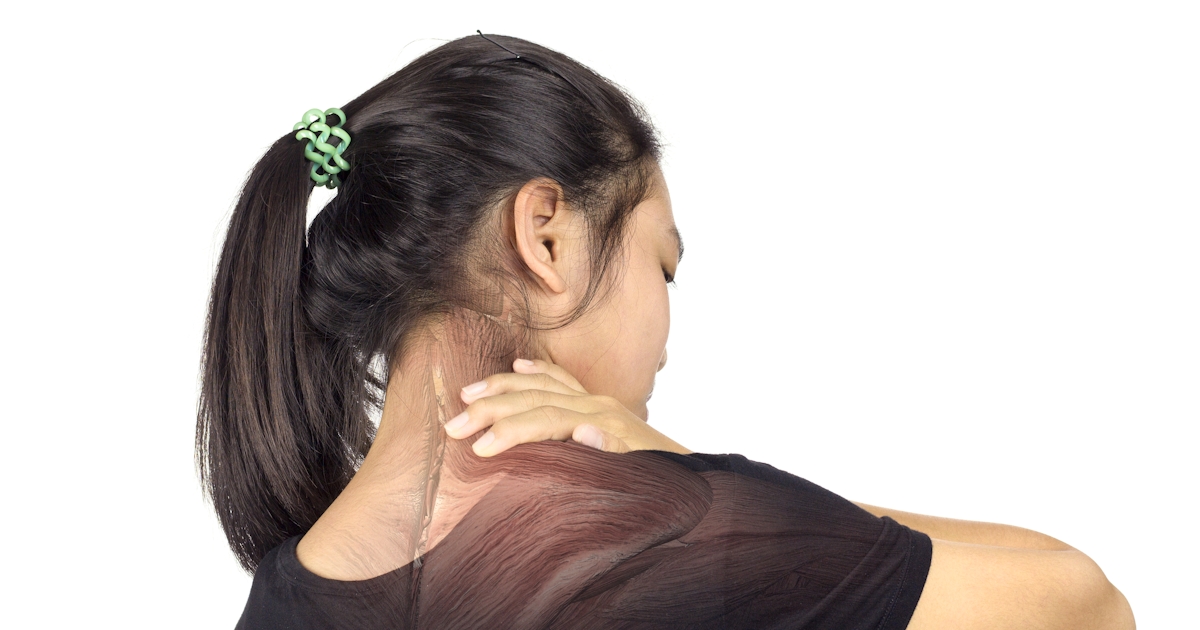 A concerned woman touches her shoulder, indicating discomfort or pain, while standing in a bright room.