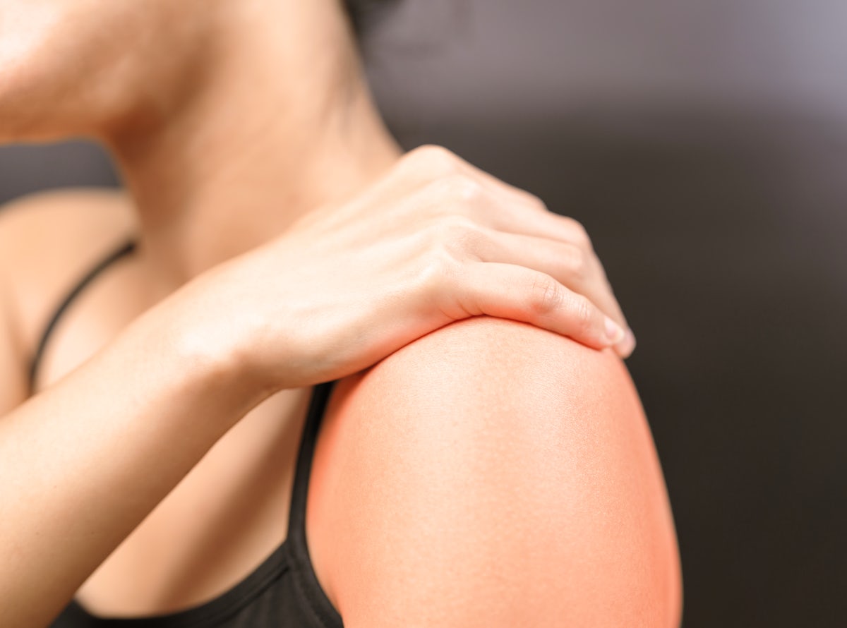 A person touching their sore shoulder, showing signs of pain or discomfort