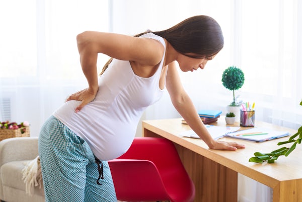 side view of a young pregnant woman holding her lower back