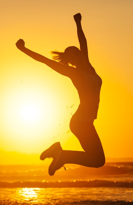 silhouette of happy female jumping in air at sunset on the beach
