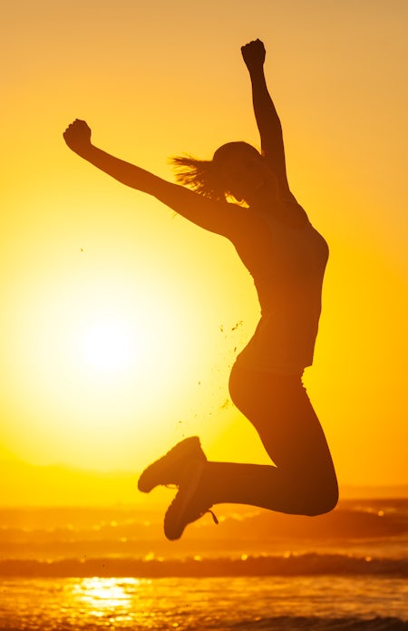 silhouette of happy female jumping in air at sunset on the beach