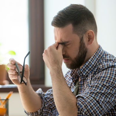 stressed young business man in front of laptop with left hand to headache migraine pain