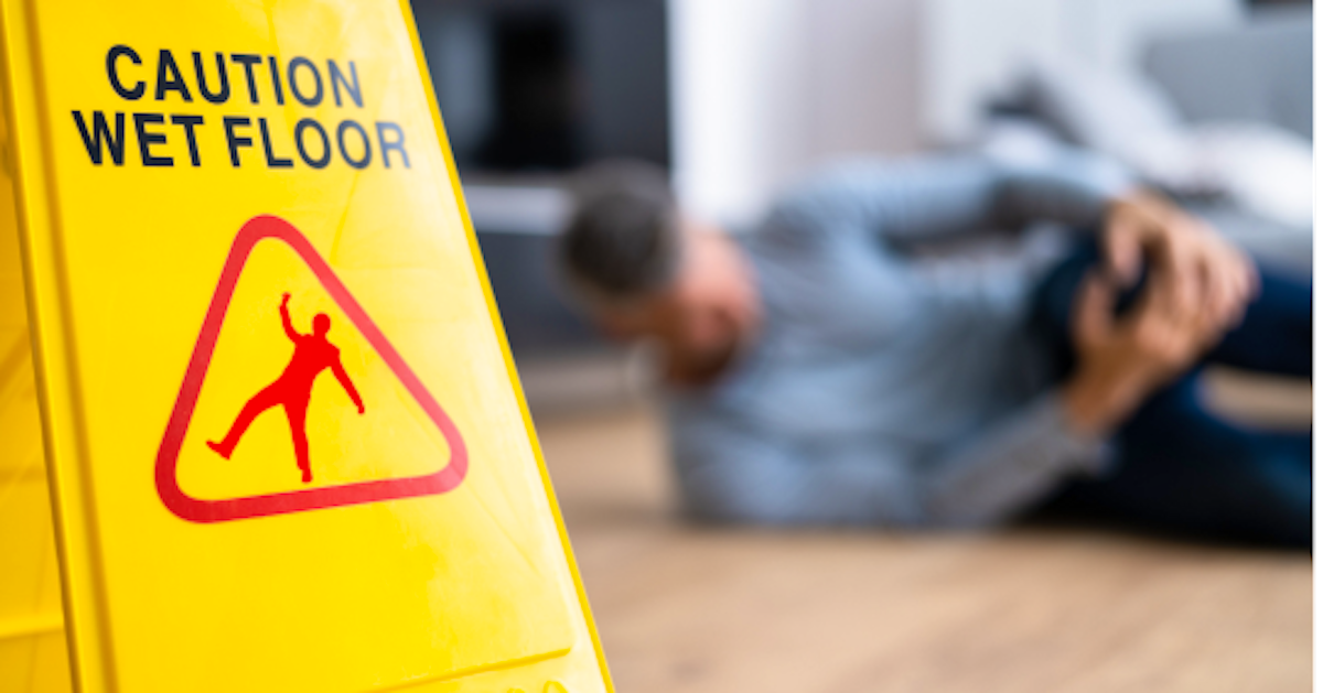 warning sign of slippery floor with someone in the background who has fallen