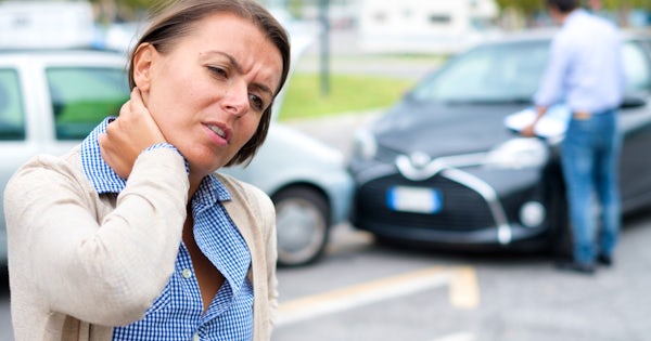white woman standing near crashed cars holding neck pain from auto injury