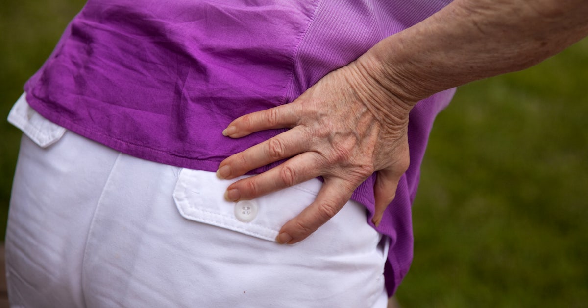 back side of woman with hand to her low back pain purple shirt
