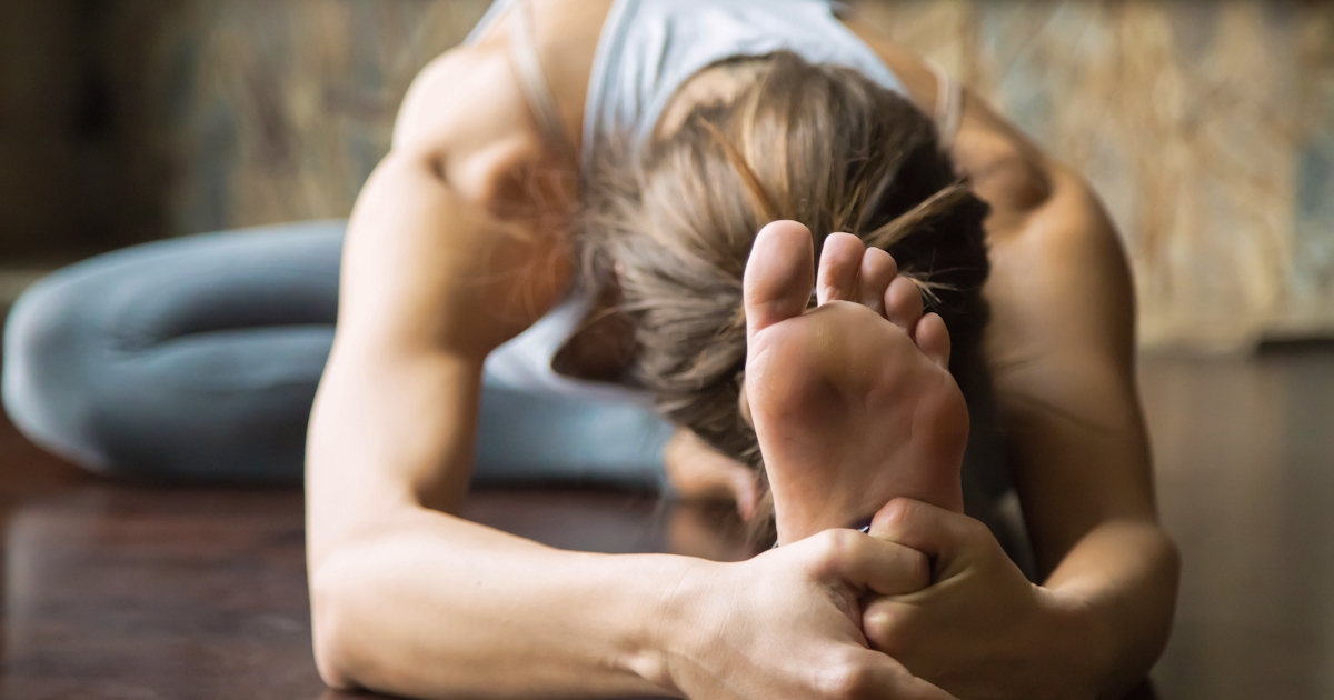 Close up young woman in Janu Sirsasana pose, home