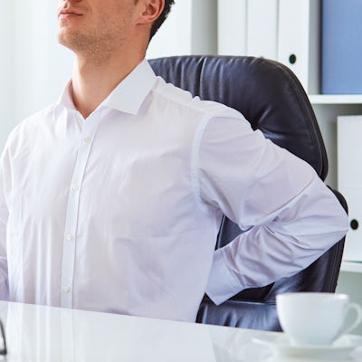 young white business man at laptop holding left arm to low back pain