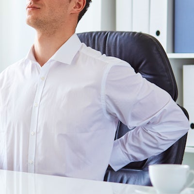 young white business man at laptop holding left arm to low back pain