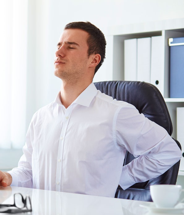 young white business man at laptop holding left arm to low back pain