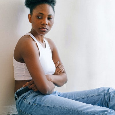 A young woman sits on the floor with her arms crossed
