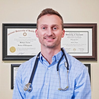  Headshot of Dr. Matthew Nuesse D.C. CME standing in front of diplomas and professional certificates